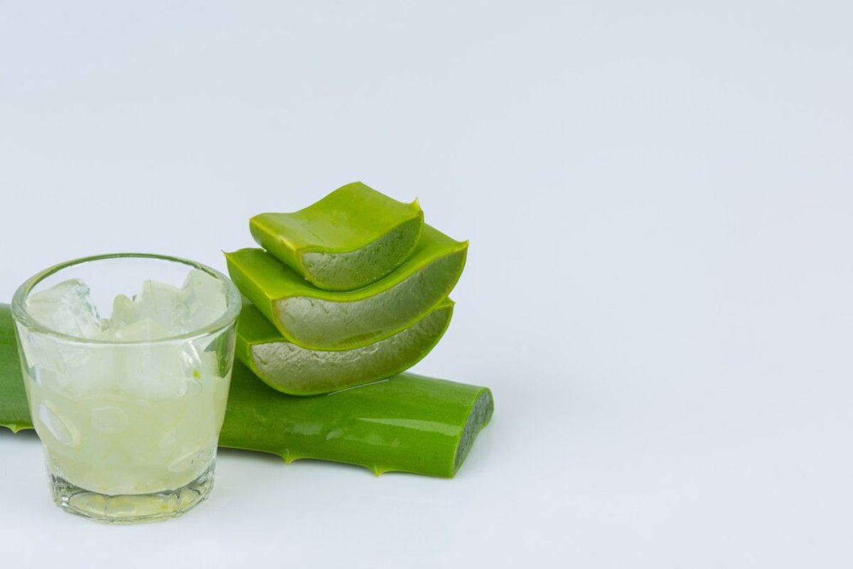 Fresh aloe vera leaves stacked beside a glass of crushed ice, highlighting the plant's natural ingredients and soothing properties.