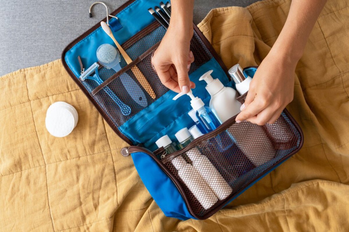 A person organizes toiletries in a blue travel case, featuring various bottles, skincare items, and tools on a yellow blanket.