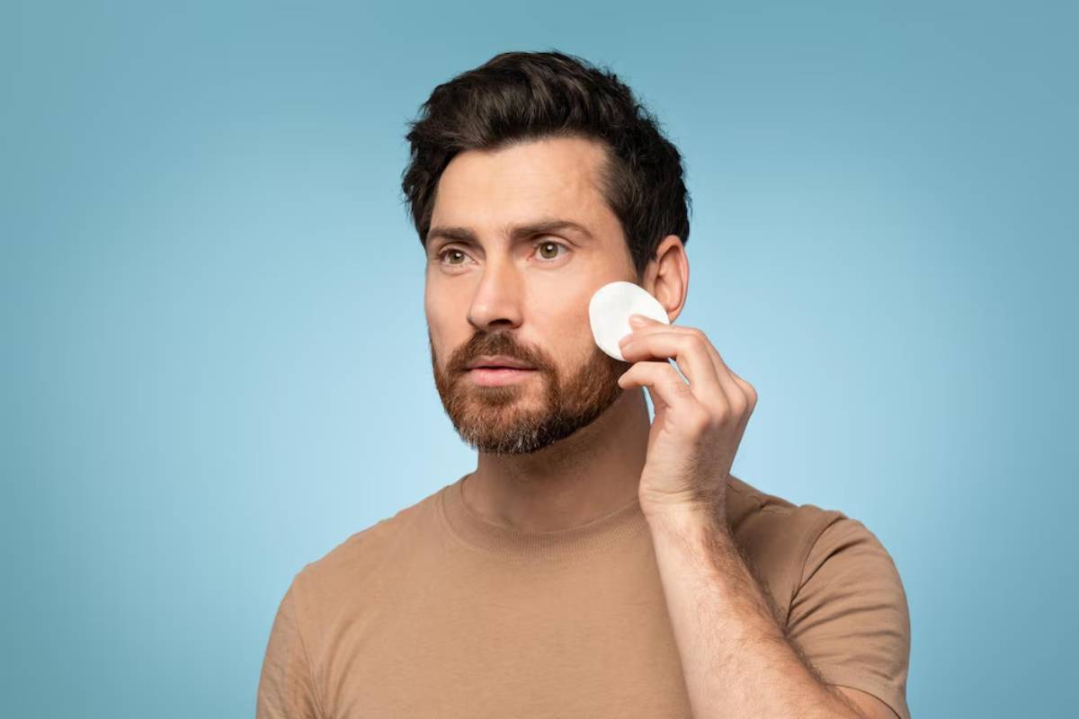A person wearing a brown t-shirt holds a phone to their ear, standing against a soft blue background.