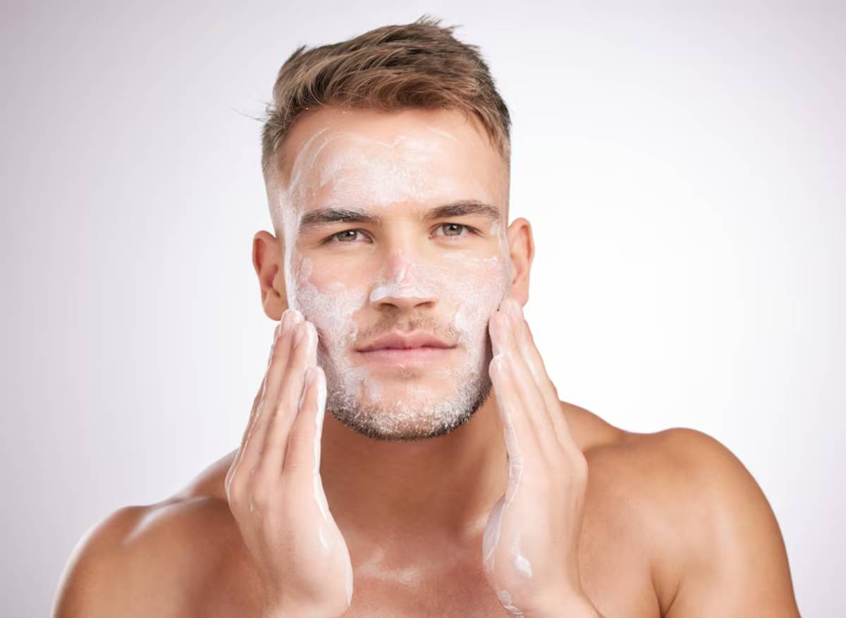 A man applies facial cleanser, his hands gently cupping his face, with a smooth, clear background highlighting his skincare routine.