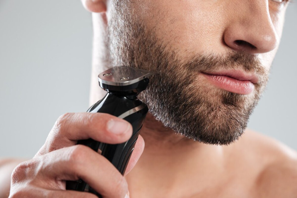 A person uses an electric trimmer to groom their facial hair against a neutral background, showcasing a grooming routine.