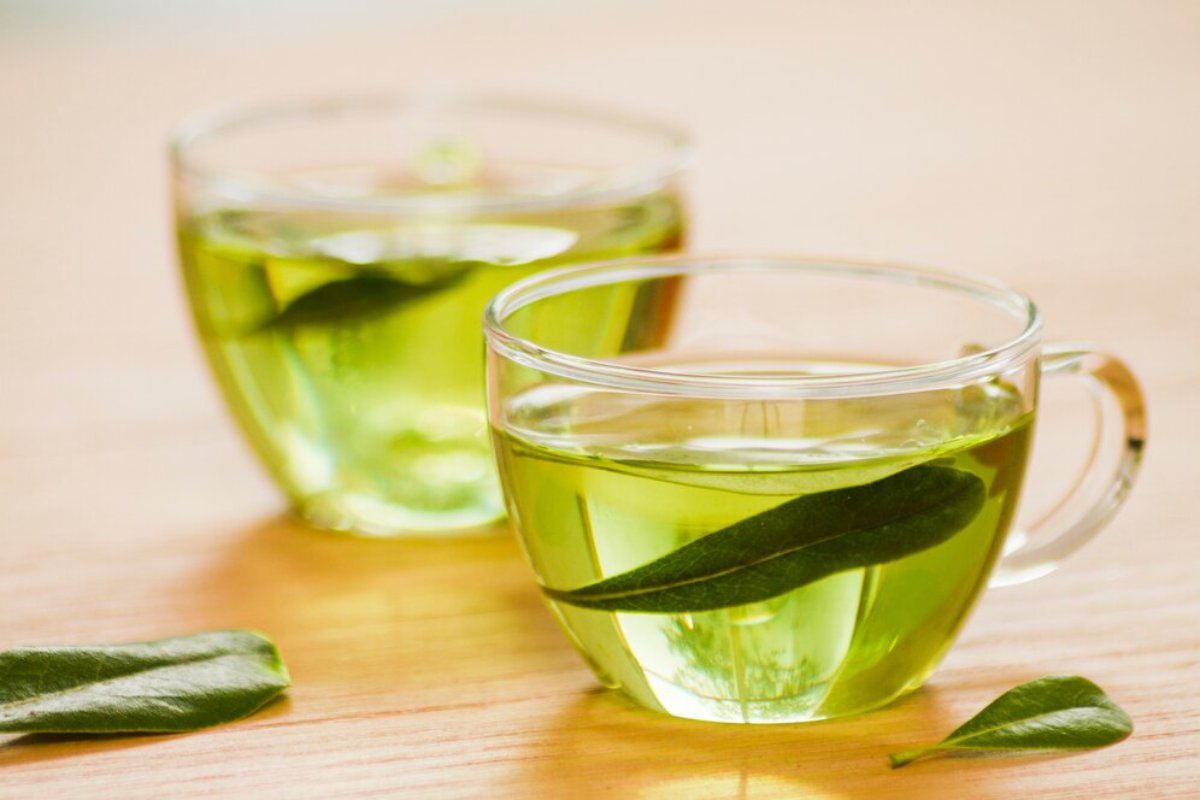 Two glass cups of green tea infused with fresh leaves, placed on a wooden surface, conveying a refreshing and healthy beverage.