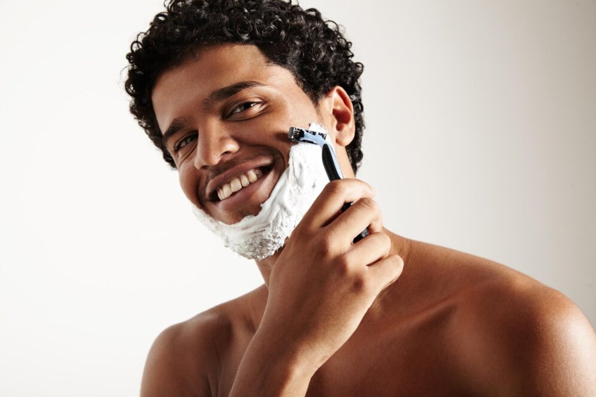 A person with curly hair holds a phone to their ear, showcasing a bare shoulder against a neutral background.