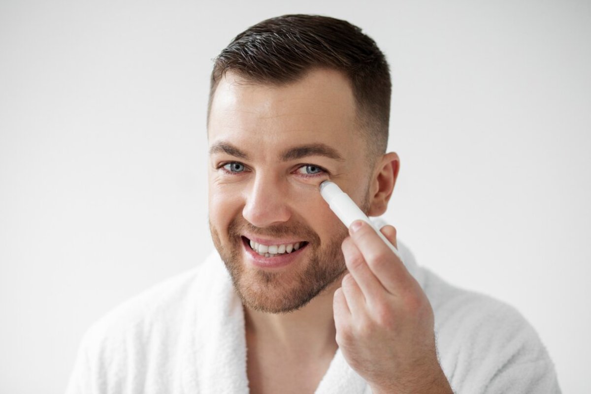 A person in a white robe applies skincare product, set against a minimalistic light background.