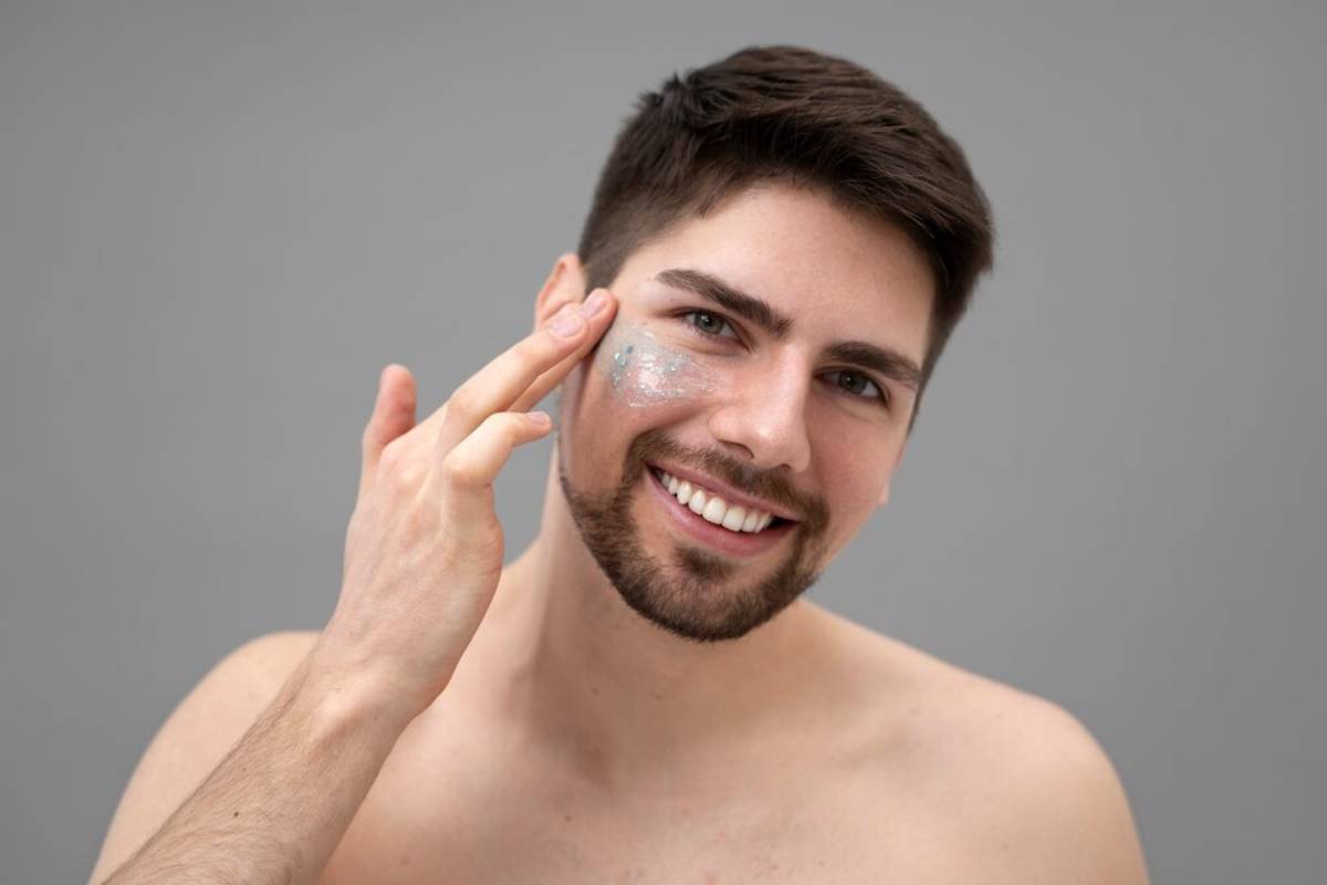 A young man with short dark hair touches his cheek, showcasing a neutral background and a bare upper body.