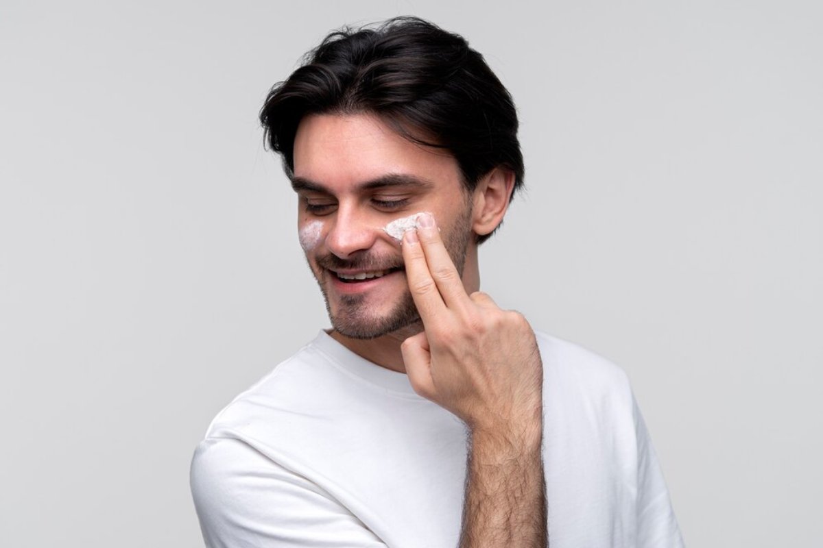 A person in a white shirt poses against a plain gray background, raising a fist to their mouth in a thoughtful gesture.