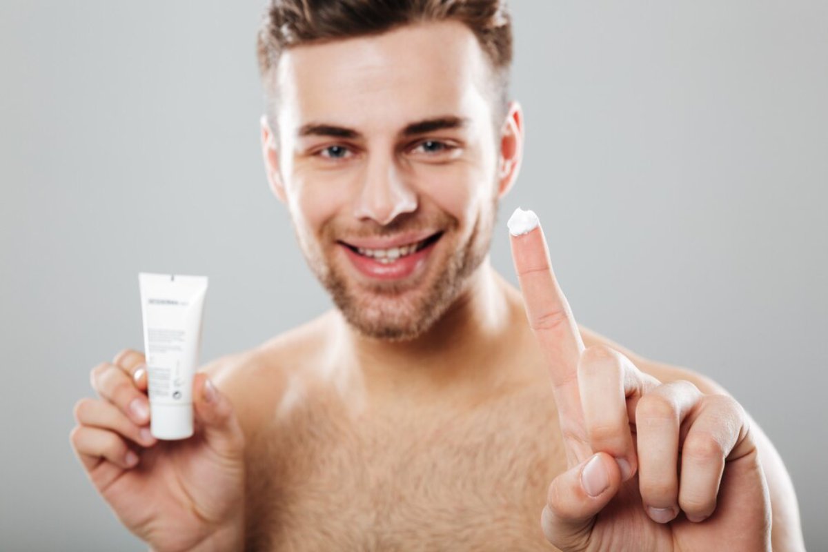 A person holds a tube of skincare cream in one hand and has a small dollop of cream on their finger, showcasing its use.