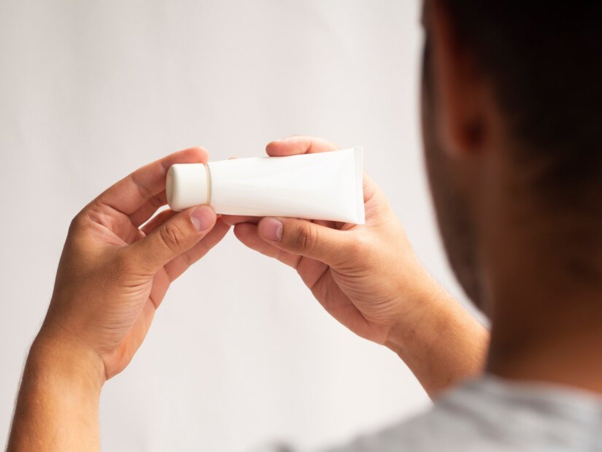 A person holding a small white skincare tube, examining it closely with a neutral background.