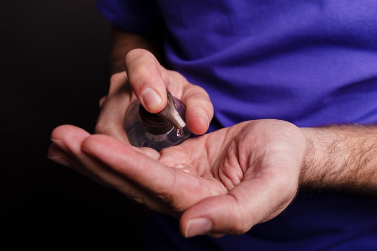 A person in a purple shirt dispenses a small amount of liquid from a pump bottle into their palm.