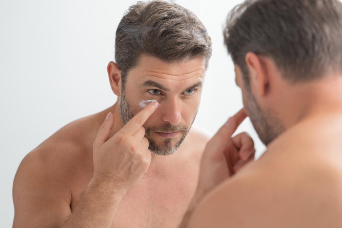 A man examines his skin closely in a mirror, showcasing a thoughtful expression in a bright, minimalist bathroom setting.