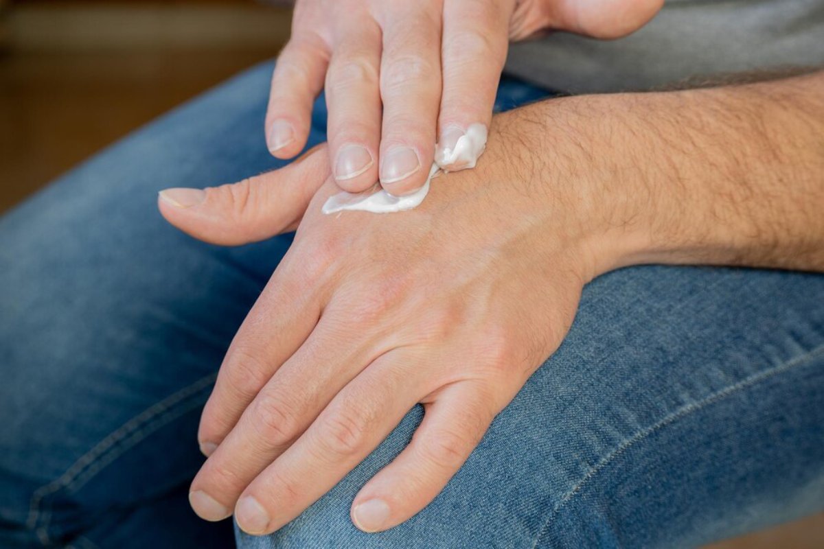 A person applying hand cream to their right hand while seated, with blue jeans visible in the background.