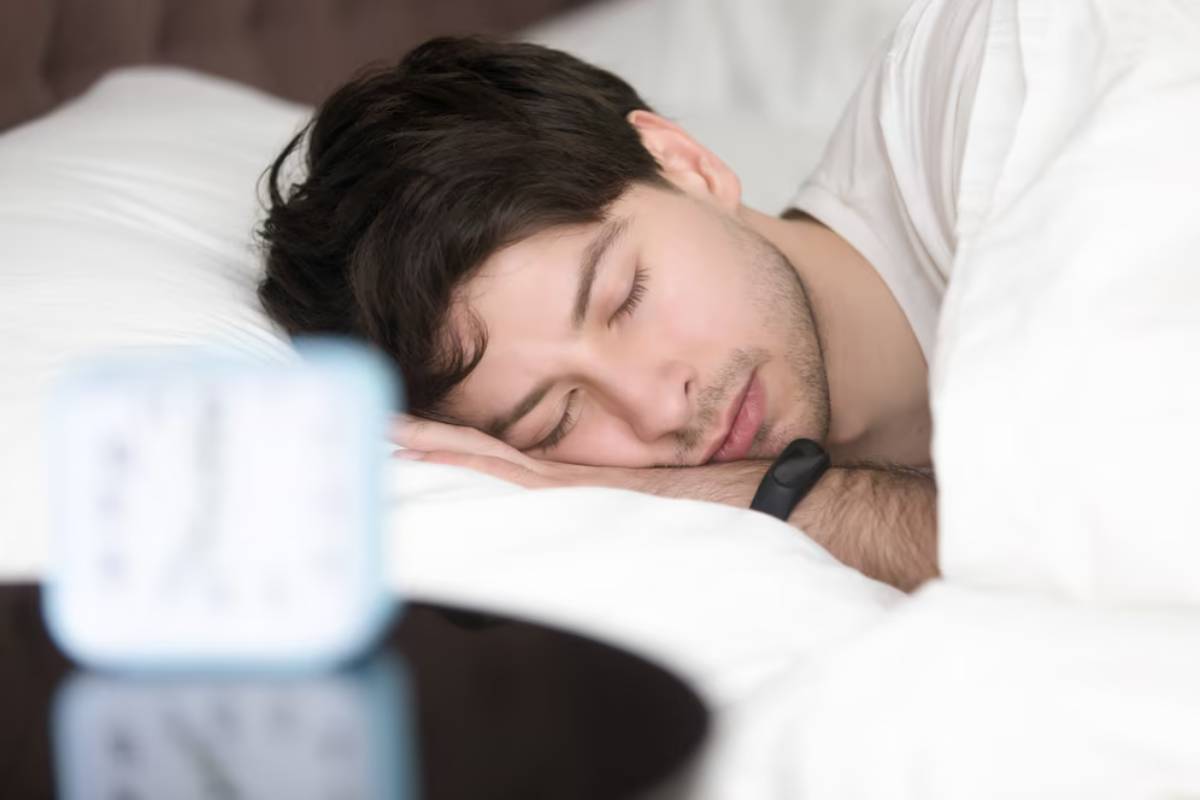 A person rests peacefully in bed, surrounded by fluffy white pillows, with a small clock on a bedside table.