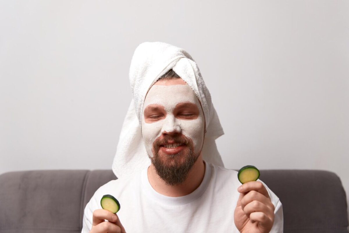 A person sitting on a couch, wearing a towel on their head and holding cucumber slices in each hand, is ready for relaxation.