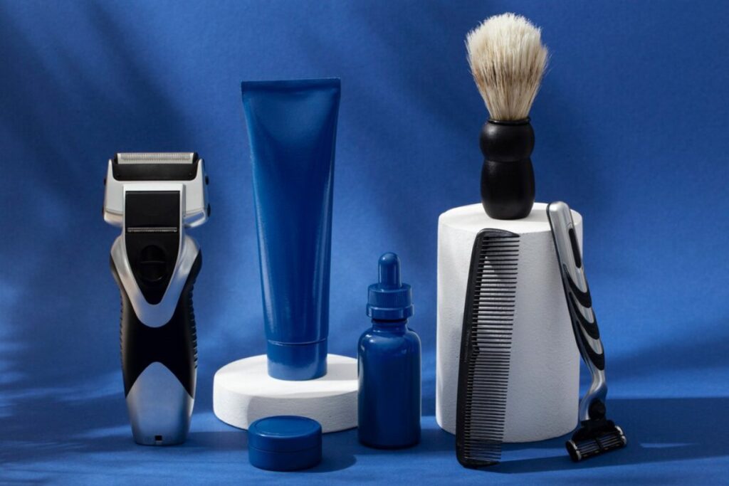 A collection of grooming products: an electric razor, cream, brush, droplet bottle, comb, and razor, against a blue backdrop.